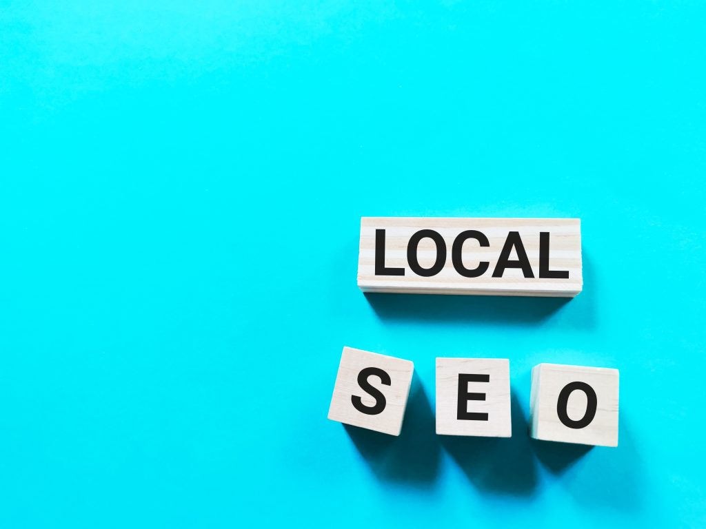 Wooden blocks spelling out "LOCAL SEO" on a bright aqua blue background, representing local search engine optimization.